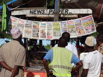 A group of men looking at a row of newspapers hung from a shop front