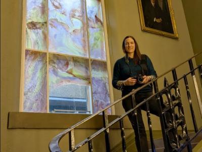 Dr Raewyn Martyn standing on a staircase in front of her artwork at the Grant Institute Cockburn Geological Museum stairwell site photographed in pale winter light. The calcium carbonate pigments from Portobello mussel shells refract light.